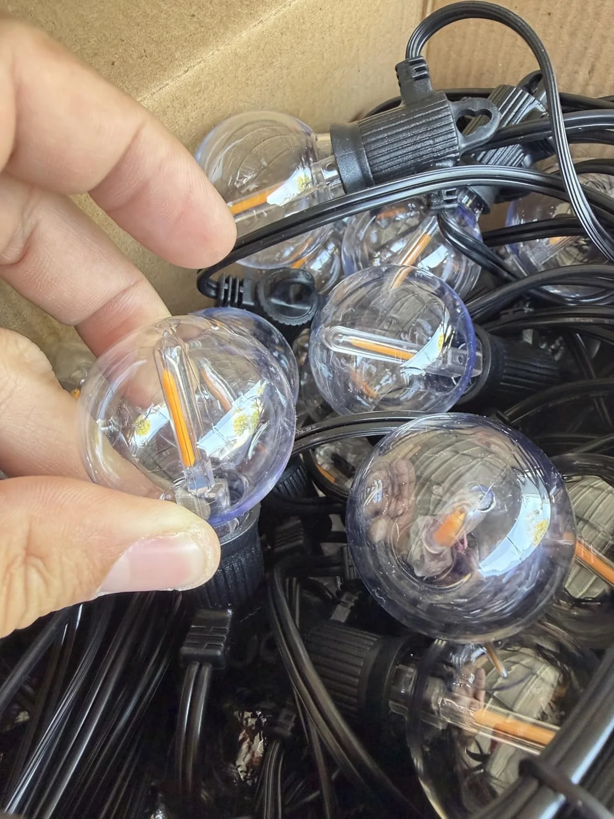 Hand holding a clear globe bulb beside coiled black string-light cable